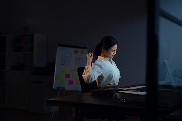 La mujer de negocios asiática tiene dolor de cuello porque usa la computadora y trabaja mucho tiempo por la noche.