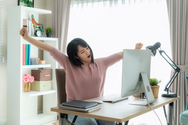 La mujer de negocios asiática trabaja desde casa y estira su cuerpo porque se siente cansada y dormida después de trabajar en la computadora, mujer inteligente que trabaja en casa.