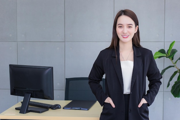 Mujer de negocios asiática con traje de falta de éxito carterista de pie y sonriendo en la oficina de trabajo