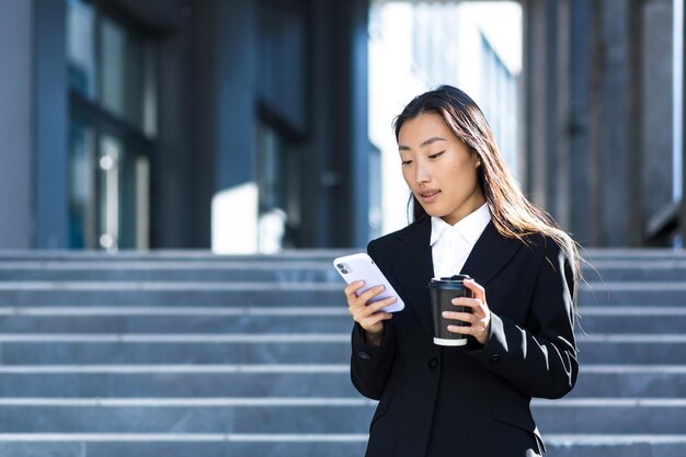 Mujer de negocios asiática usando el teléfono, una mujer cerca del centro de oficinas, caminando por la ciudad durante un descanso