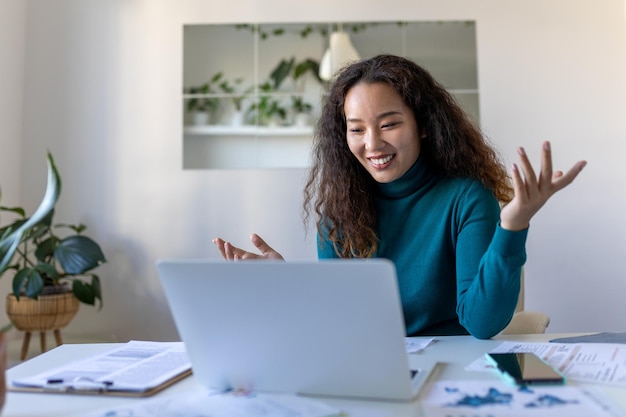 Mujer de negocios asiática en una videollamada mientras está sentada en su escritorioCaptura recortada de una mujer joven atractiva que usa su computadora portátil para hacer una videollamada en casa