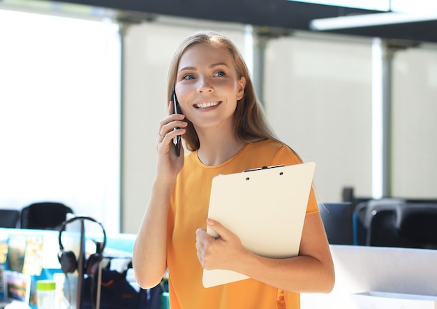 Mujer de negocios atractiva hablando con colegas por teléfono móvil mientras está sentado en el escritorio de la oficina.