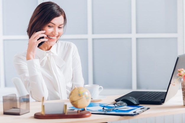 Mujer de negocios atractiva hablando por teléfono y trabajando en el escritorio en la oficina