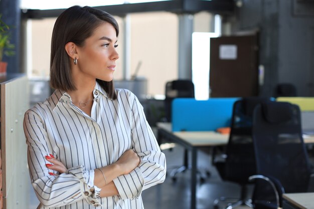 Mujer de negocios atractiva en ropa casual elegante mirando a otro lado mientras está de pie en la oficina.