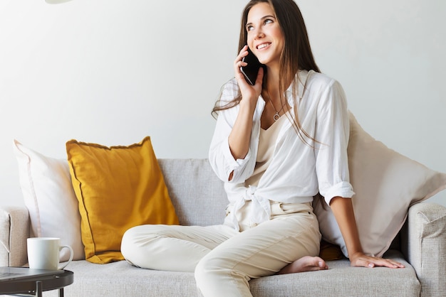 Foto mujer de negocios atractiva está sentada en el sofá y hablando por teléfono celular, negociando por teléfono.