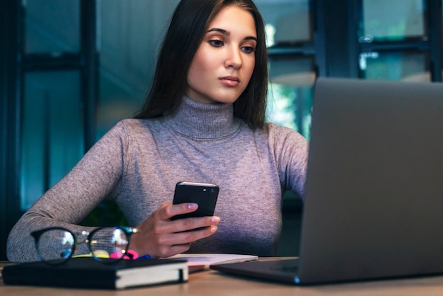 Mujer de negocios atractiva se sienta a la mesa frente a la computadora portátil, trabaja de forma remota mientras está en la cafetería.