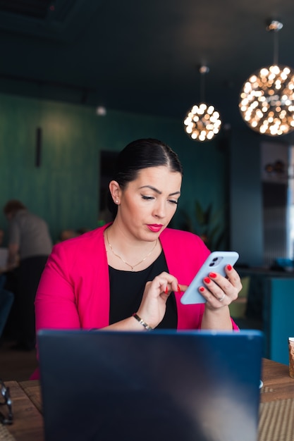 Mujer de negocios atractiva con teléfono móvil en la cafetería