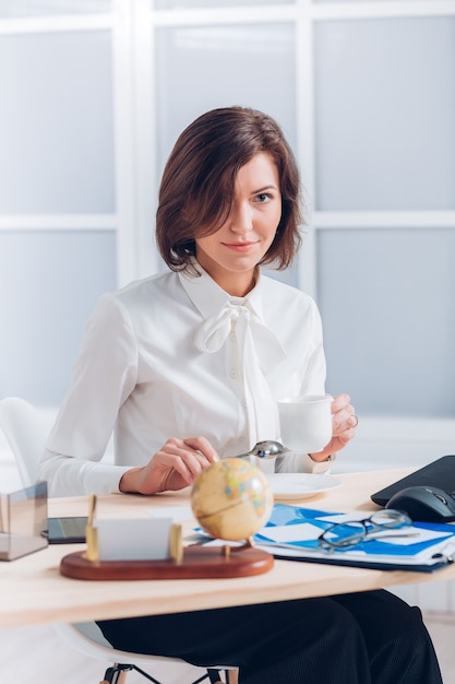 Mujer de negocios atractiva tomando café y trabajando en el escritorio en la oficina