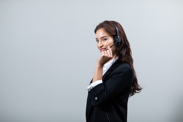 Mujer de negocios atractiva en trajes y auriculares sonríe mientras trabaja aislado