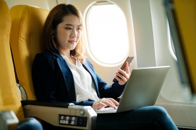 Mujer de negocios en un avión trabaja en el uso de computadora portátil y teléfono