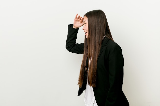 Mujer de negocios bastante china joven que mira lejos manteniendo la mano en la frente.