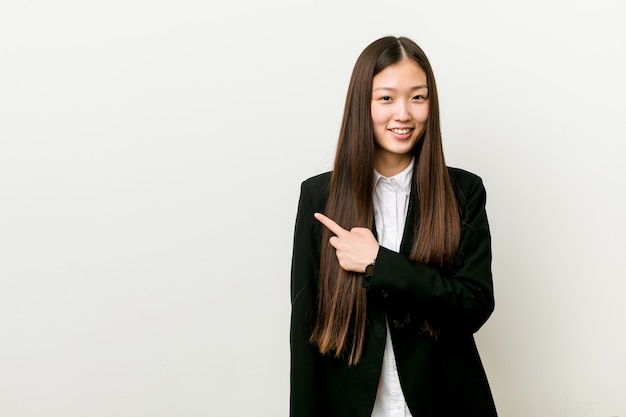 Mujer de negocios bastante china joven que sonríe y que señala a un lado, mostrando algo en el espacio en blanco.