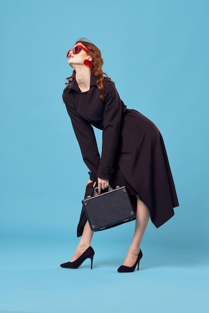 Mujer de negocios bonita en fondo azul de las gafas de sol del estilo elegante de la capa negra
