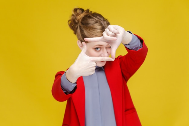 Mujer de negocios de cabeza roja en traje rojo que muestra el signo de framecrop