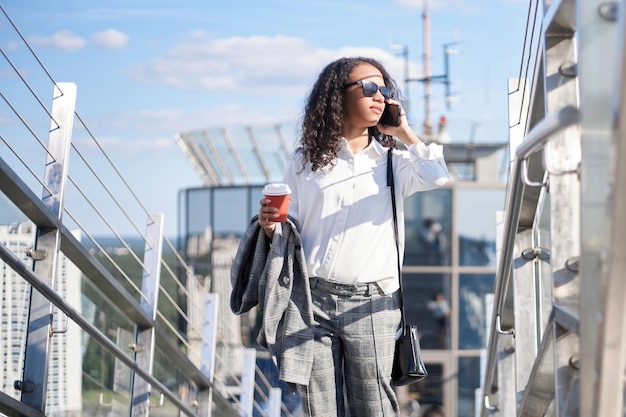 Mujer de negocios con un café para llevar hablando por un teléfono inteligente