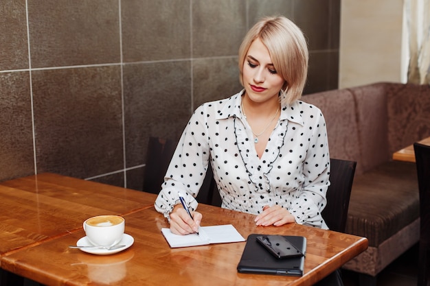Mujer de negocios en café sentado y escribiendo en el cuaderno