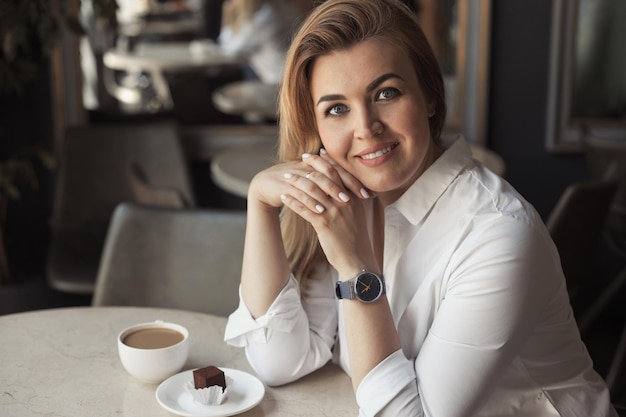Mujer de negocios con camisa blanca de oficina con cabello rubio bebiendo una taza de café en un café