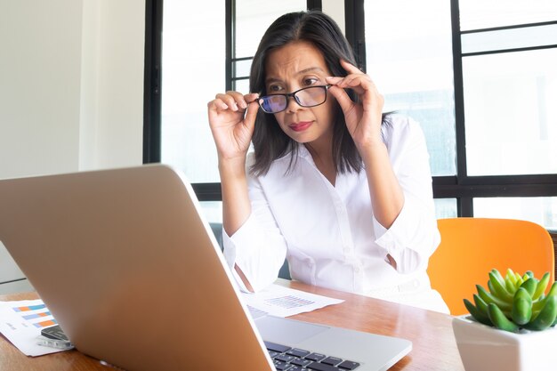 Mujer de negocios en camisa blanca Use gafas sentado en el lugar de trabajo