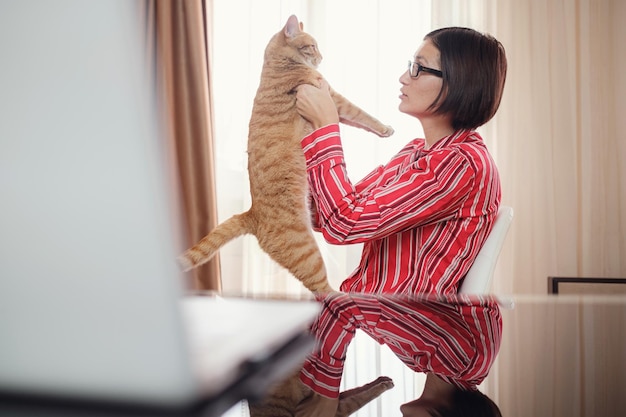 Mujer de negocios con una camisa roja con un gato jengibre en casa