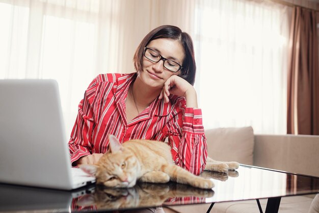 Mujer de negocios con una camisa roja con un gato jengibre en casa