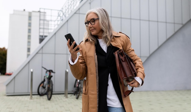 Mujer de negocios canosa adulta mayor se apresura a una reunión y mira un teléfono móvil de un año