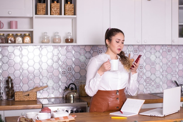 mujer de negocios en casa en la cocina resuelve negocios en el teléfono funciona en línea