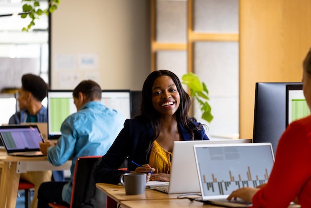 Foto mujer de negocios casual feliz y colegas diversos que trabajan usando computadoras en la oficina. oficina casual, trabajo en equipo, comunicación, negocios y trabajo, inalterados.