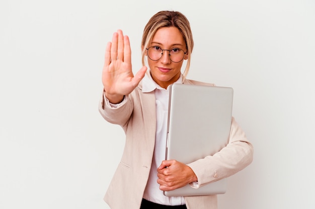 Foto mujer de negocios caucásica joven que sostiene una computadora portátil aislada en blanco que se coloca con la mano extendida que muestra la señal de stop, que le impide.