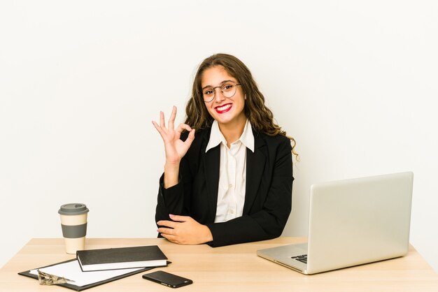 Mujer de negocios caucásica joven que trabaja en su escritorio aislado alegre y confiado que muestra el gesto aceptable.