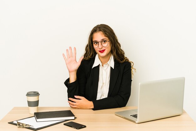 Mujer de negocios caucásica joven que trabaja en su escritorio sonriendo alegre mostrando el número cinco con los dedos.