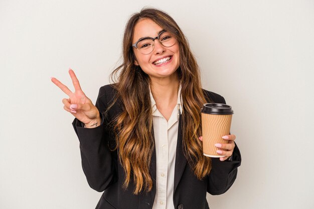 Mujer de negocios caucásica joven sosteniendo un café para llevar aislado sobre fondo blanco alegre y despreocupada mostrando un símbolo de paz con los dedos.