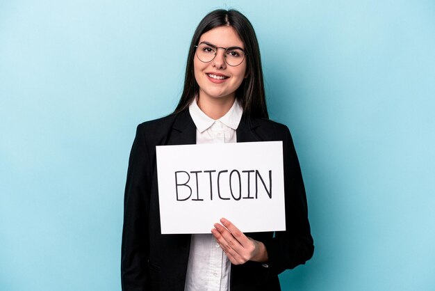 Mujer de negocios caucásica joven sosteniendo un cartel de bitcoin aislado sobre fondo azul feliz sonriente y alegre