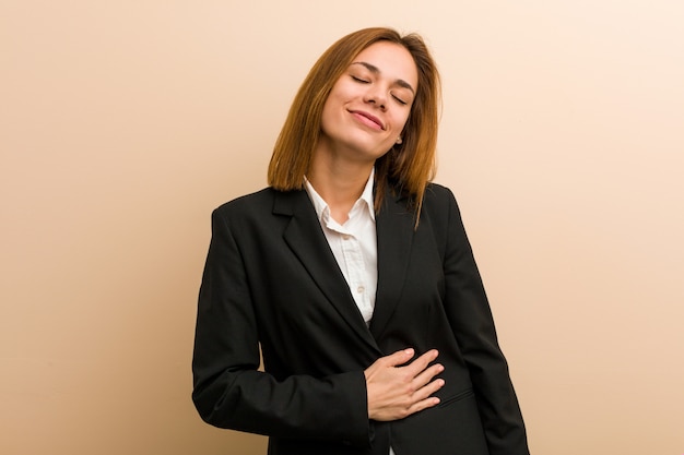 La mujer de negocios caucásica joven toca la panza, sonríe suavemente, comiendo y concepto de la satisfacción.