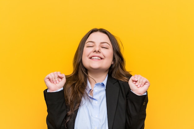 Mujer de negocios caucásica de talla grande joven levantando el puño, sintiéndose feliz y exitoso. Concepto de victoria