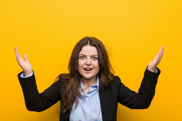 Mujer de negocios caucásica de talla grande joven que recibe una agradable sorpresa, emocionado y levantando las manos