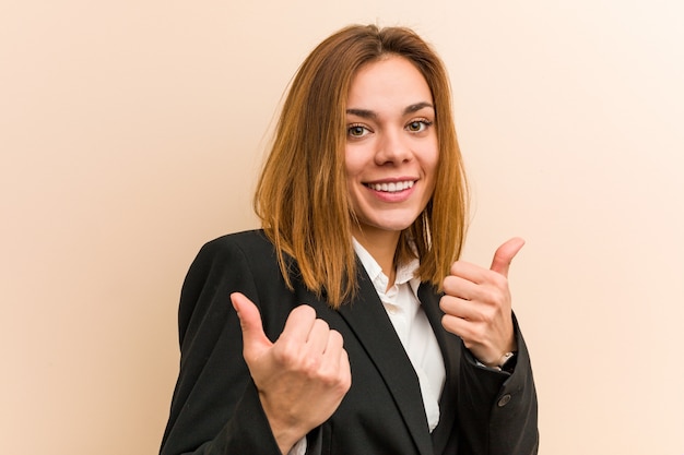 Mujer de negocios caucásico joven levantando ambos pulgares, sonriente y confiado.