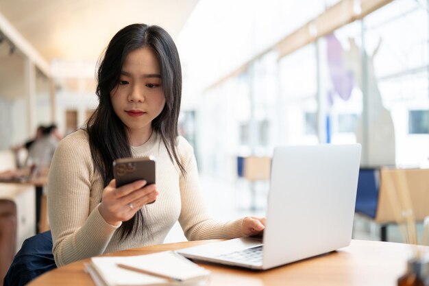 Una mujer de negocios se centra en leer mensajes en su teléfono mientras trabaja a distancia en una cafetería