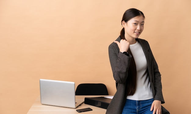 Mujer de negocios china en su lugar de trabajo apuntando hacia un lado para presentar un producto