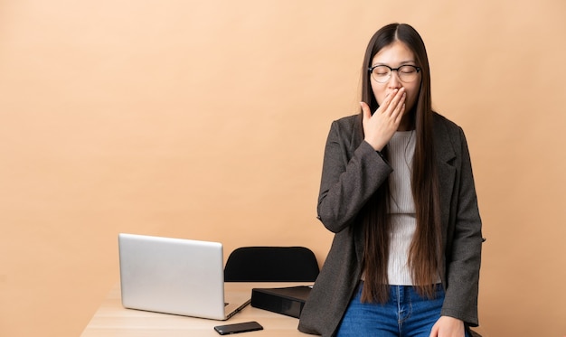 Mujer de negocios china en su lugar de trabajo bostezando y cubriendo la boca abierta con la mano