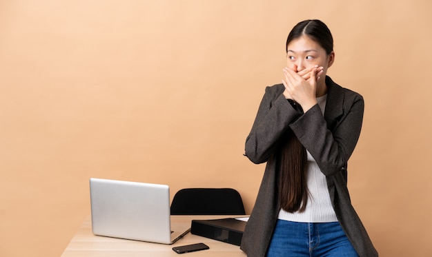 Mujer de negocios chinos en su lugar de trabajo cubriendo la boca y mirando hacia un lado