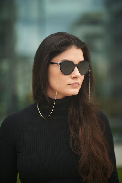 Mujer de negocios en la ciudad Una dama caucásica elegante y atractiva usa gafas de sol oscuras de moda con accesorios de cadena Retrato al aire libre de una mujer segura de sí misma