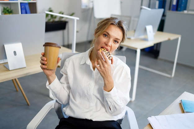 Mujer de negocios comiendo galletas y bebiendo café