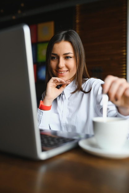 Foto mujer de negocios confiada que busca currículum vitae en el sitio a través de una computadora portátil mientras está sentado en el restaurante durante las vacaciones de trabajo. gerente de proyecto femenino utilizando aplicaciones en el dispositivo portátil, descansando en el café