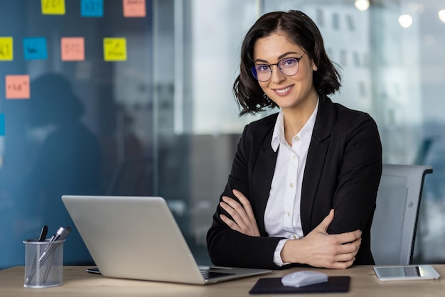 Una mujer de negocios confiada sentada en su escritorio de la oficina con una computadora portátil y coloridas notas adhesivas en el