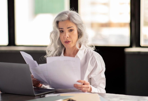 Mujer de negocios confundida mirando documentos en papel y facturas en el cargo
