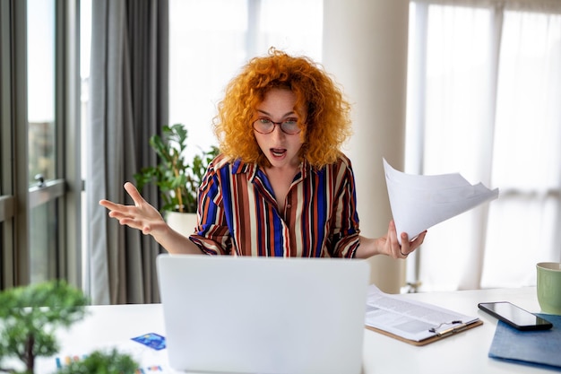 Mujer de negocios conmocionada que usa una computadora portátil en casa mirando la pantalla charlando leyendo o escribiendo correos electrónicos sentada en el sofá estudiante haciendo la tarea trabajando en un proyecto de investigación en línea