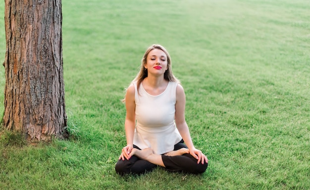 Mujer de negocios descansando después de un duro día en el césped, relajándose y haciendo yoga