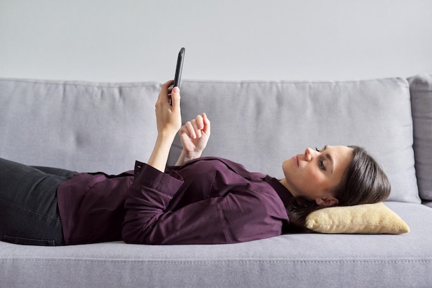 Mujer de negocios descansando en la oficina en el descanso. Mujer relajada tumbada en el sofá leyendo un smartphone. Área de relajación de la oficina, preocupación por la comodidad de los empleados