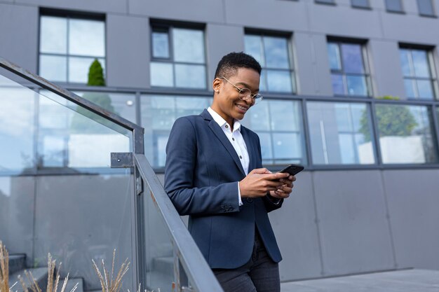 La mujer de negocios disfruta de la diversión del celular y la sonriente mujer de negocios afroamericana fuera de la oficina en traje de negocios