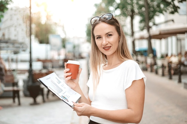 Mujer de negocios con un documento financiero y un café para llevar de pie en una calle de la ciudad